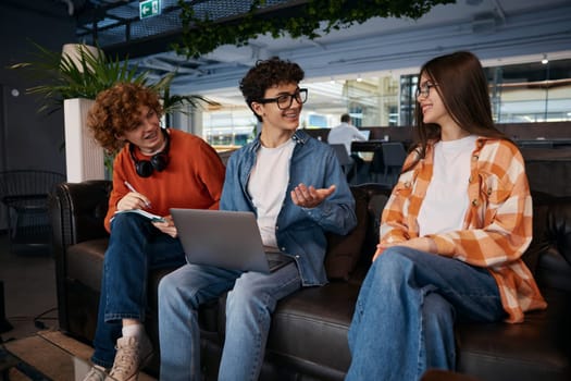 Team of teenagers sitting on sofa in office. Three young employees discussing new work project