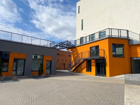 A contemporary street view showcasing orange building, large windows, and sidewalk with wooden benches, in autumn season.