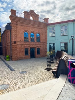 A contemporary street view showcasing a modern building with white brick walls, large windows, and sidewalk with wooden benches, and greenery.