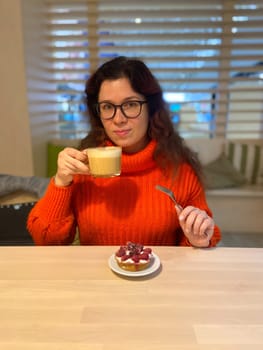 Woman eating tartelette of cherry or cake and drink coffee, close up.