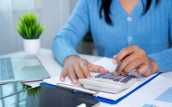 Businesswoman hand working with finances about cost and calculator and laptop with tablet on desk at office in morning light, Business accounting concept, Calculating or checking balance.