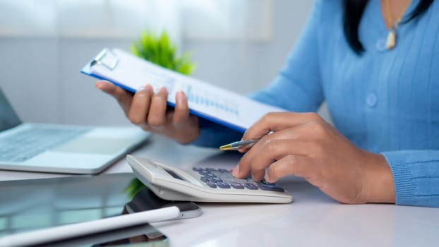 Businesswoman hand working with finances about cost and calculator and laptop with tablet on desk at office in morning light, Business accounting concept, Calculating or checking balance.