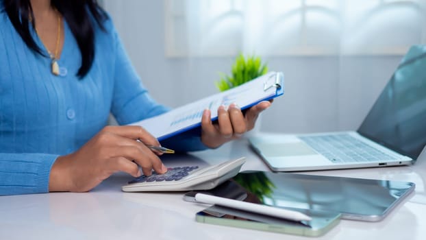 Businesswoman hand working with finances about cost and calculator and laptop with tablet on desk at office in morning light, Business accounting concept, Calculating or checking balance.