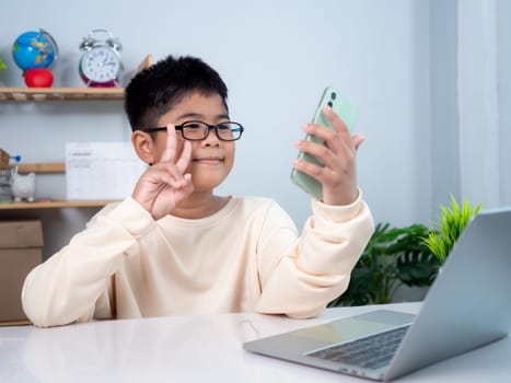 Asian student boy using computer and phone learning. Educational of tech concept, Staying at home, Presenting a modern educational way of life. Virtual internet online class from school teacher.