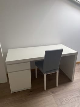 Minimalist workspace with a white desk and a gray chair on a wooden floor. Simple design offers a clean and organized environment perfect for productivity and focus.