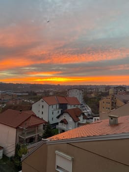 Sunset over a suburban neighborhood with vibrant orange hues illuminating the sky. Rooftops and distant cityscape create a harmonious blend with the natural beauty of the evening light.