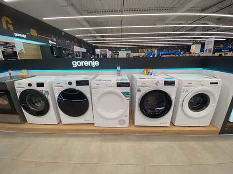 Row of modern washing machines is displayed in an electronics store, showcasing the latest models with sleek designs and advanced features. Under bright lights, the machines stand out against the store contemporary interior.