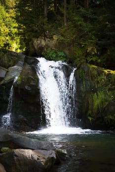 A beautiful waterfall in a rocky canyon is surrounded by a green autumn forest. Ukraine, Zakarpattya.