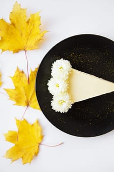 creamy cheesecake on a black plate decorated with yellow maple leaves.