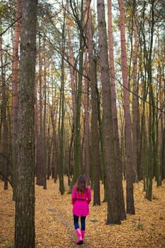 girl in a raincoat and pink rubber boots walking in an autumn forest.