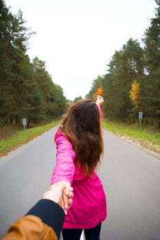 the girl is standing on the road holding a yellow leaf.