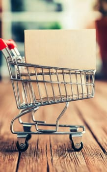A miniature shopping cart holds a brown parcel, symbolizing online shopping and delivery services. Black Friday sale concept with place for text.