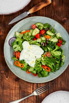 Salad of greens, tomatoes, cucumbers and fresh cream cheese Burrata. Burrata salad with vegetables on rustic wooden table