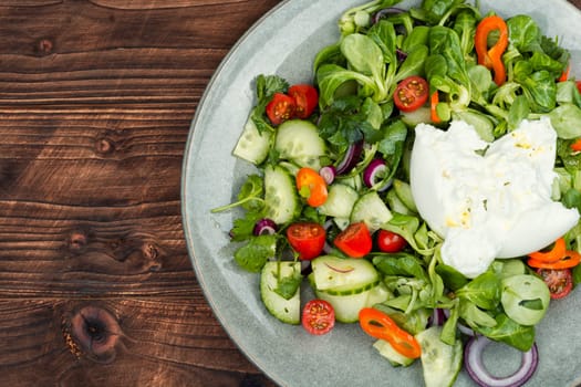 Salad of greens, tomatoes, cucumbers and fresh cream cheese Burrata. Burrata salad with vegetables on rustic wooden table
