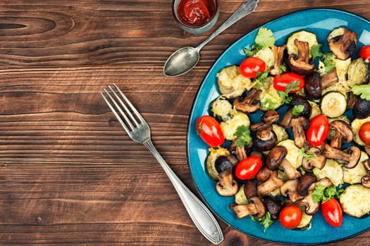 Mushrooms, zucchini and tomatoes baked in the oven on rustic wooden table. Space for text.