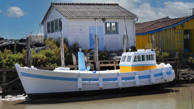A small white boat with blue trim sits next to a house. island of Oleron, France
