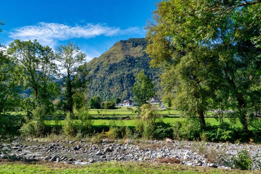 A mountain range with a small town in the distance. The trees are green and the sky is blue, Laruns, France
