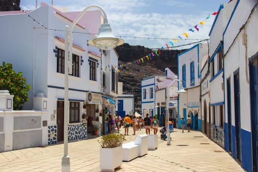 Puerto de las Nieves, island of Gran Canaria, Spain – 20 Jul 2024. Tourists and locals on the streets with typical white-blue romantic architecture port town.