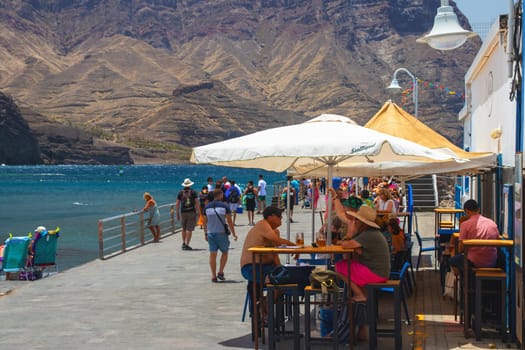 Puerto de las Nieves, island of Gran Canaria, Spain – 20 Jul 2024. Tourists and locals on the streets with typical white-blue romantic architecture port town.