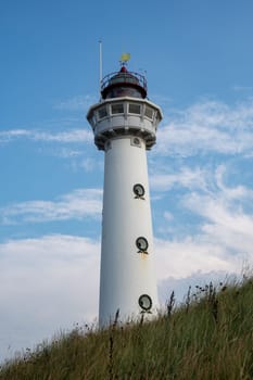 The approx. 28 m high white lighthouse J.C.J. van Speijk in Egmond aan Zee, North Holland, Netherlands, in the sand dunes with beach grass, blue sky and clouds