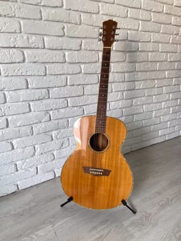 Wooden acoustic guitar stands elegantly against a textured white brick wall, creating a harmonious blend of music and art. Instrument craftsmanship.