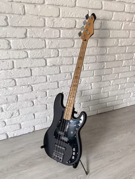 Sleek black electric bass guitar stands poised against a textured white brick wall, capturing the essence of modern music and style. The contrast between the dark instrument and the light surroundings highlights its contemporary design and musical allure