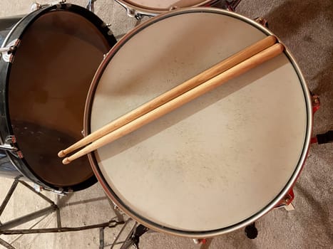 Pair of wooden drumsticks rests on a snare drum, inviting rhythm and energy. Musical experience waiting to unfold in this intimate setting.