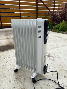 White oil-filled radiator stands outside on a concrete surface, prepared to provide warmth on a chilly day. Portable design makes it a practical heating solution for various environments.