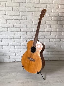 Wooden acoustic guitar stands elegantly against a textured white brick wall, creating a harmonious blend of music and art. Instrument craftsmanship.