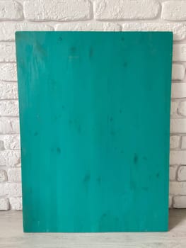 Vibrant turquoise wooden panel contrasts vividly against a textured white brick wall, highlighting its smooth finish and bold color. Embodies a refreshing blend of modernity and simplicity, making it visually striking.