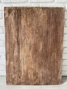 Rustic wooden panel leans gracefully against a textured white brick wall, showcasing its rich grain patterns and natural warmth. Contrast between the organic wood and the structured brick provides a harmonious blend of nature and architecture.