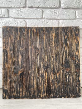 Rustic wooden panel leans gracefully against a textured white brick wall, showcasing its rich grain patterns and natural warmth. Contrast between the organic wood and the structured brick provides a harmonious blend of nature and architecture.