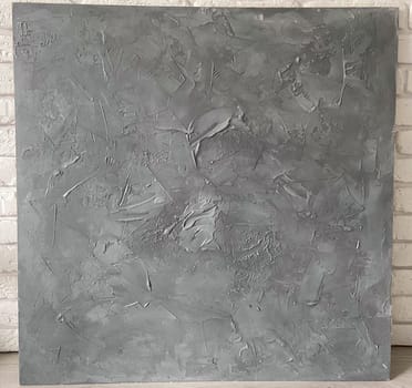 Textured gray canvas leans against a white brick wall, offering a stark contrast and highlighting the intricate details within the artwork. Artistic blend of the canvas meets the structured simplicity of the urban backdrop.