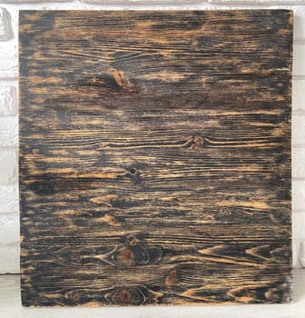 Rustic wooden panel leans gracefully against a textured white brick wall, showcasing its rich grain patterns and natural warmth. Contrast between the organic wood and the structured brick provides a harmonious blend of nature and architecture.