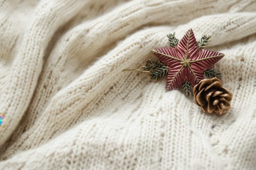 A soft cream colored knitted blanket draped elegantly with a decorative star ornament and a pinecone resting nearby.