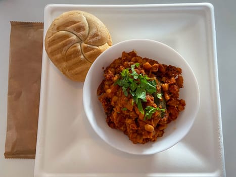 Delicious meal featuring a hearty bowl of stew garnished with herbs, served alongside fresh bread and a frothy coffee, is presented on a clean white tray. Inviting combination of flavors and textures perfect for a satisfying breakfast or lunch.