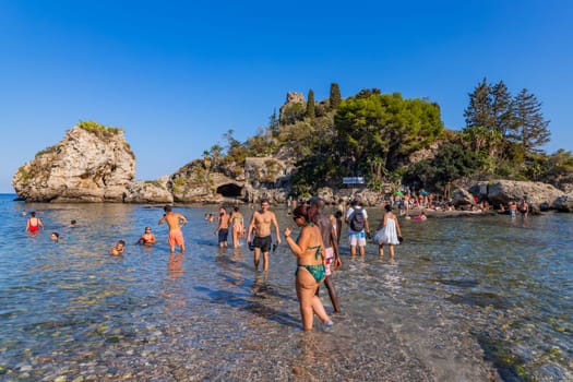Taormina, Italy - August 11, 2024: People on the beach of Taormina with Isola Bella island on the background. Sicilia, Italy