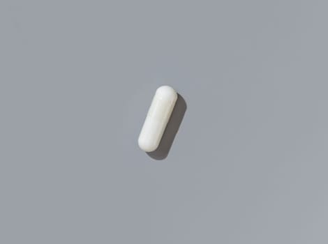 White medical capsule on grey top view, hard shadows. Preventive medicine and healthcare, taking dietary supplements and vitamins. Minimal composition
