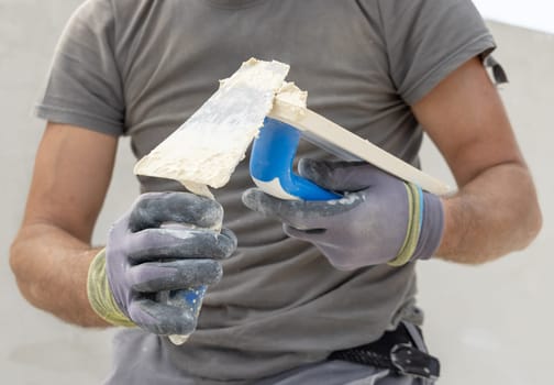 Craftsman puts plaster or grout on a float closeup. Men in grey work clothes and dirty gloves during construction or renovation process
