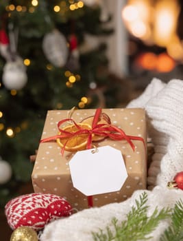 Santa Claus hands put a present decorated with dried fruits near cosy heart and sweater against Christmas tree lights, close up. Winter holidays atmosphere with grandfarthers hands laying a gift box