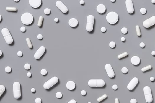Mix of white medical capsules and pills with open space in the middle on grey top view. Medicinal treatment. Taking dietary supplements. Assorted pharmaceutical products