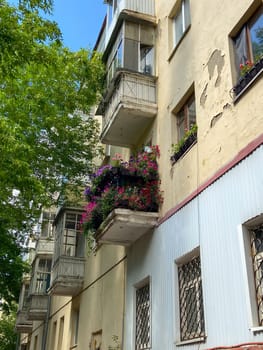 Vibrant urban apartment building stands tall, with colorful flowers adorning its balconies against a backdrop of lush green trees and a bright blue sky. Harmonious blend of nature and city life, highlighting a touch of beauty in everyday surroundings.