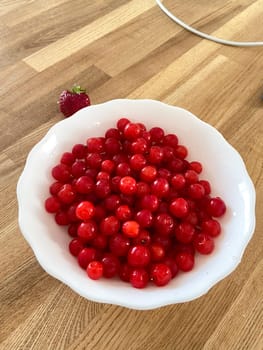 Collection of vibrant red berries sits elegantly in a white bowl, creating a striking contrast against a wooden background. Simple composition showcases the freshness and natural appeal of the fruit.