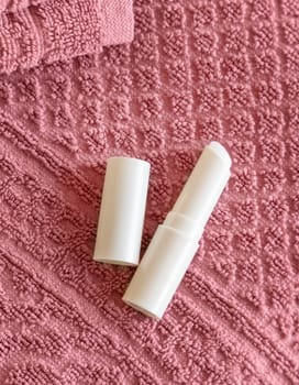 Opened white blank lip balm stick on dark grey folded towels, top view, cosmetic mockup. Lifestile scene with lipcare product, everyday personal care
