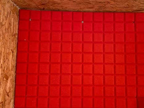 Vibrant red acoustic paneling against wood creates a striking visual contrast in this minimalist interior. Texture and color combination enhance the sense of modern design and functionality.