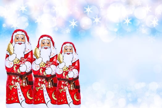Christmas card template. Various cheerful wrapped chocolate Santa Claus over festive abstract blurred winter landscape. Xmas and New Year gift sweets. Macro.