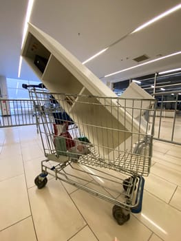 Large piece of furniture is precariously balanced in a shopping cart inside a spacious, modern mall. The unusual sight contrasts everyday shopping tasks with unexpected logistical challenges.