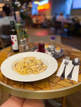 Delicious plate of pasta graces a wooden table in a vibrant cafe, offering a perfect mix of culinary delight and casual dining atmosphere. The lively background adds a sense of connection and shared experience, capturing the essence of modern dining.