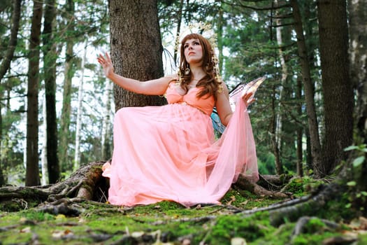 A beautiful elf with a crown and wings sits in a forest