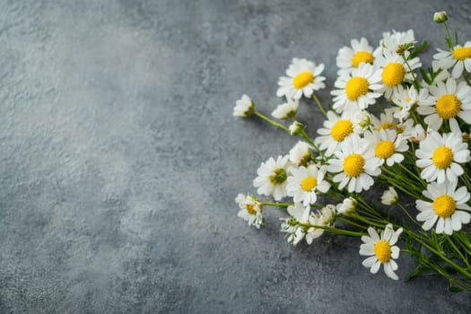 A bunch of fresh daisies with white petals and yellow centers are elegantly arranged on a gray textured surface showcasing their natural beauty.